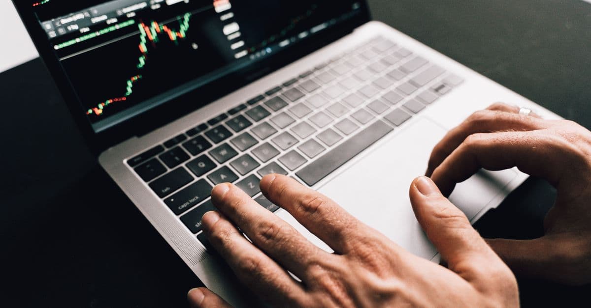 Close-up of hands typing on a laptop with stock market graphs, ideal for finance or business themes.